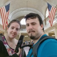 Iván y Laura en Ellis Island Immigrant Building con audioguía y fondo decorado con banderas de EE.UU.